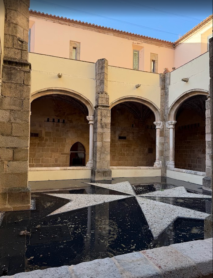 An eight-pointed Maltese cross set in stone, reflected in shallow water